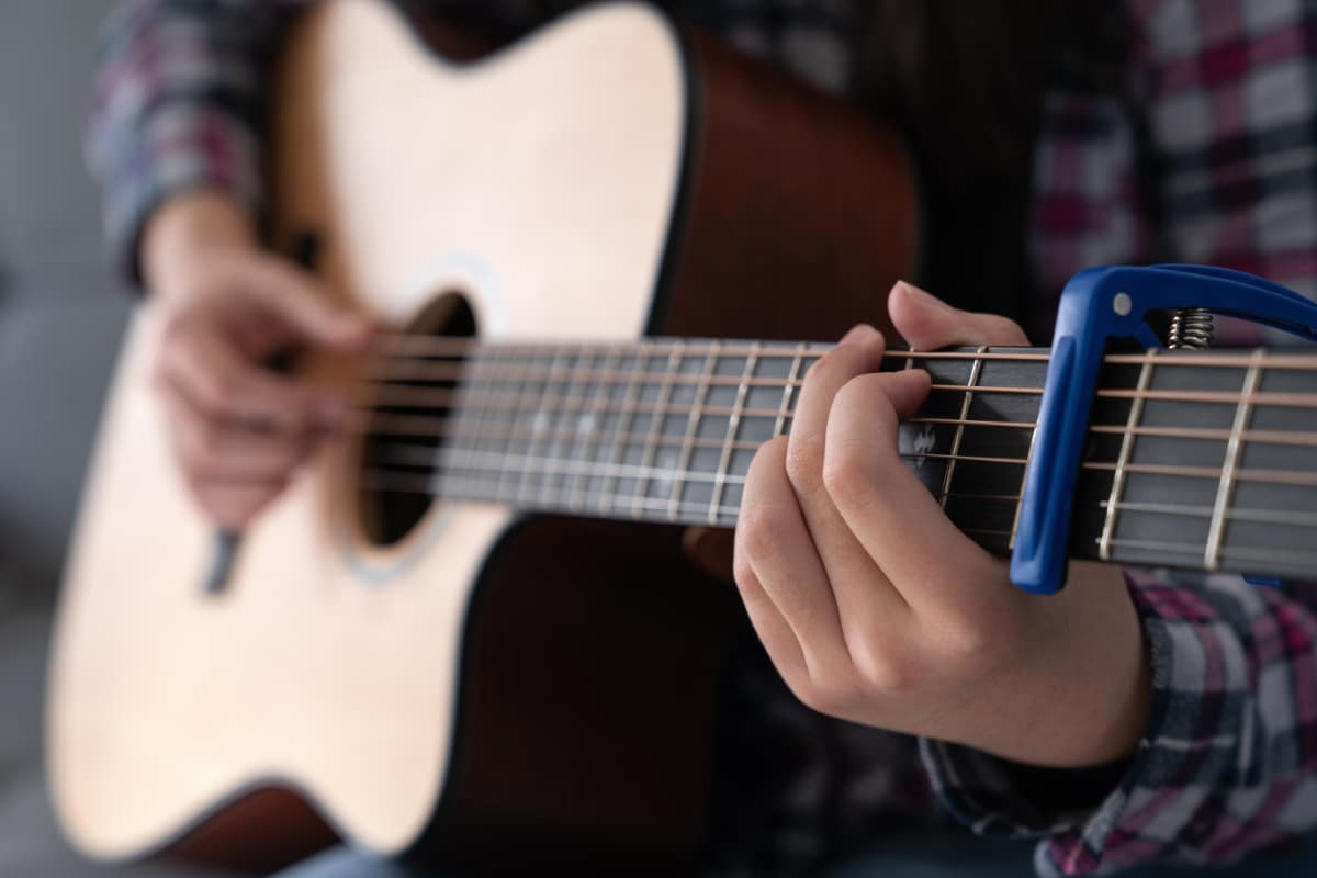 A woman's hands playing guitar and using a capo to transpose keys