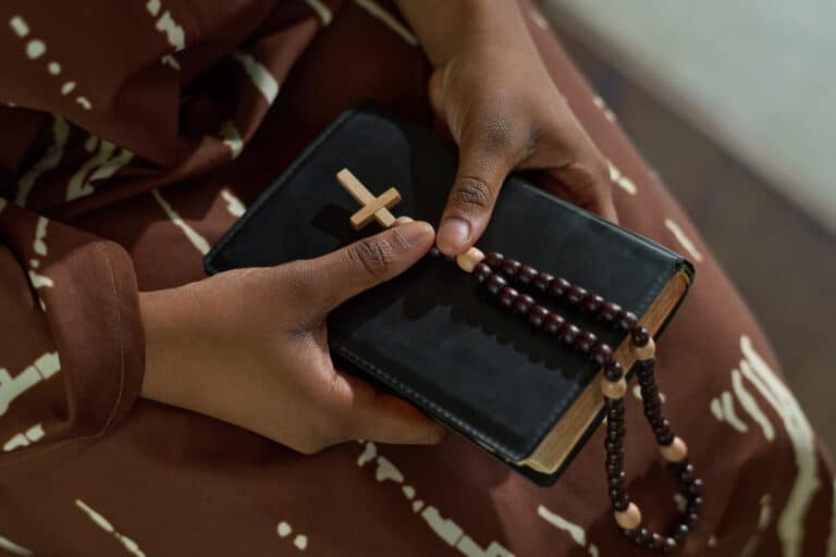 Hands of a young African American woman holding a Bible and a rosary as part of an article discussing celebrating diversity on Pentecost