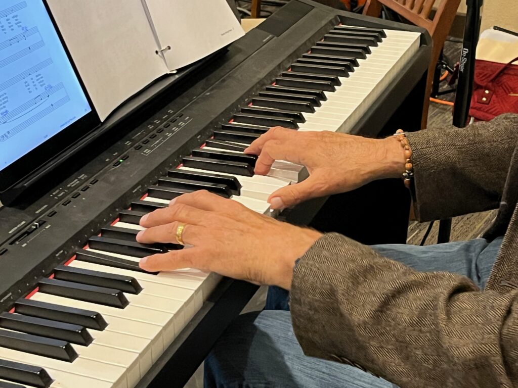 Close-up of hands playing a digital piano with sheet music, contributing to ensemble music.